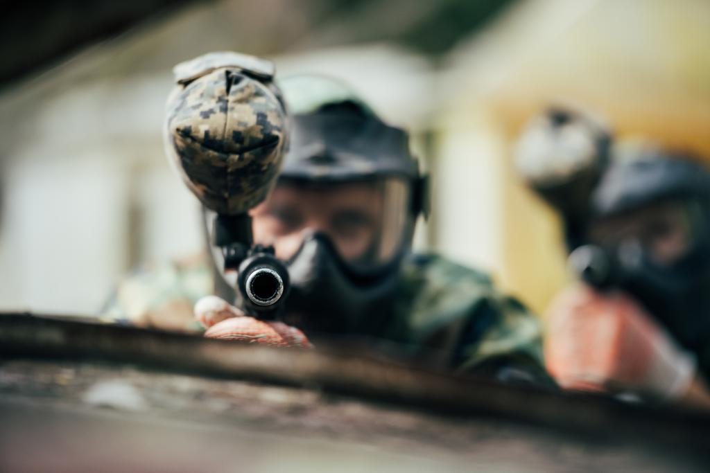 вибірковий фокус команди пейнтболу в уніформі та захисних масках, спрямованих на пістолети-кулемети на відкритому повітрі
 - Фото, зображення