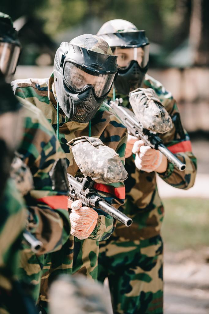 paintball players in goggle masks and camouflage uniform holding paintball guns outdoors  - Photo, Image