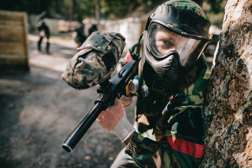 selective focus of male paintball player in goggle mask and camouflage with paintball gun outdoors  - Photo, Image