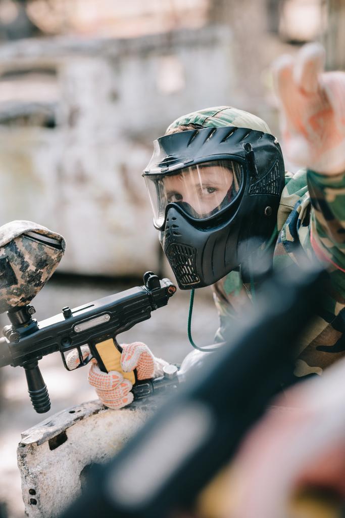 Ανδρική paintballer ΜΑΣΚΑ μάσκα και καμουφλάζ κρατώντας όπλο δείκτη και δείχνοντας με το δάχτυλο σε εξωτερικούς χώρους  - Φωτογραφία, εικόνα