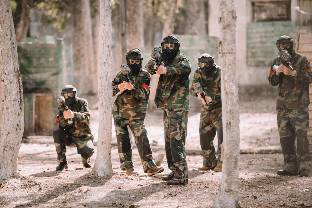 Paintball team in uniform en beschermende maskers gericht door paintball guns buitenshuis - Foto, afbeelding
