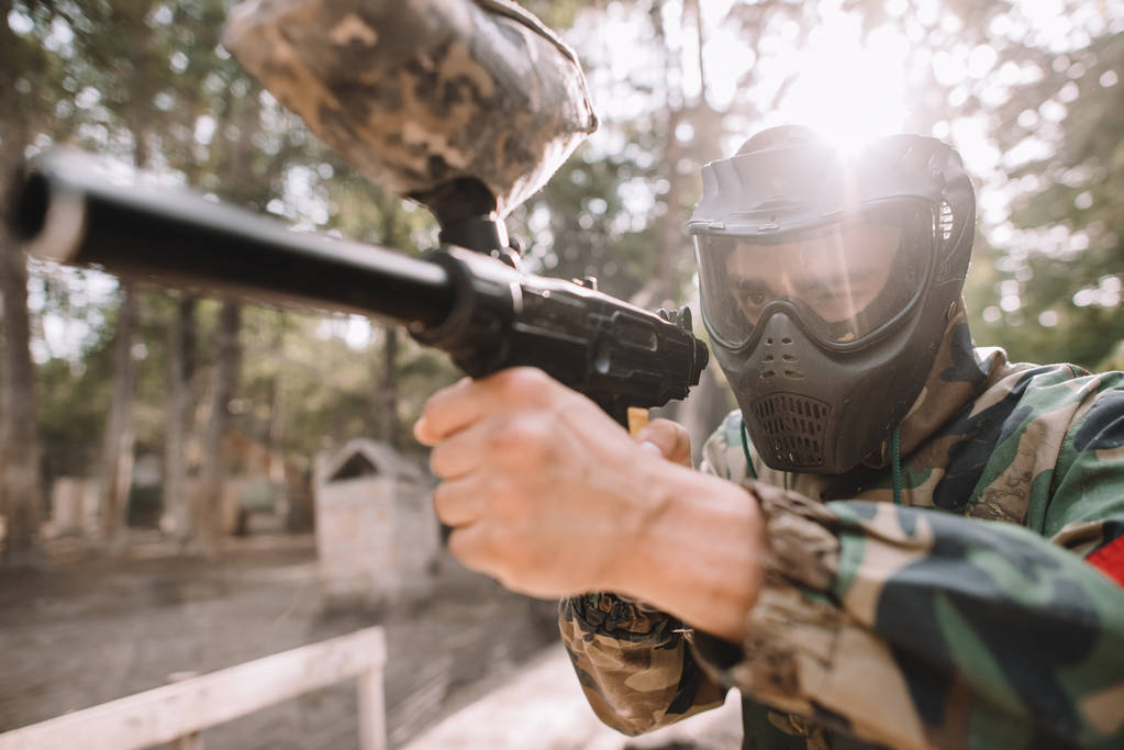 gericht mannelijke paintball speler in goggle masker en camouflage gericht door paintball pistool buitenshuis - Foto, afbeelding