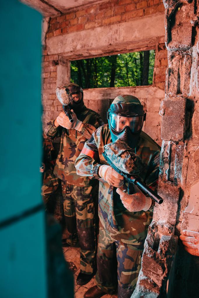 paintball team in uniform and protective masks playing standing with paintball guns in abandoned building - Photo, Image