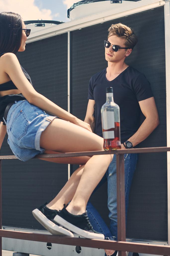 Multikulturelles Paar verbringt Zeit mit Flasche Alkohol auf dem Dach - Foto, Bild