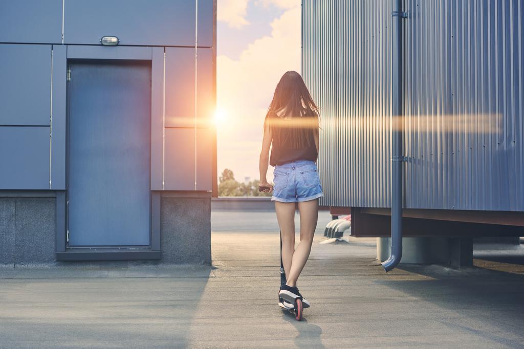 vista trasera de la joven mujer montando scooter en el techo con rayos de sol
 - Foto, Imagen
