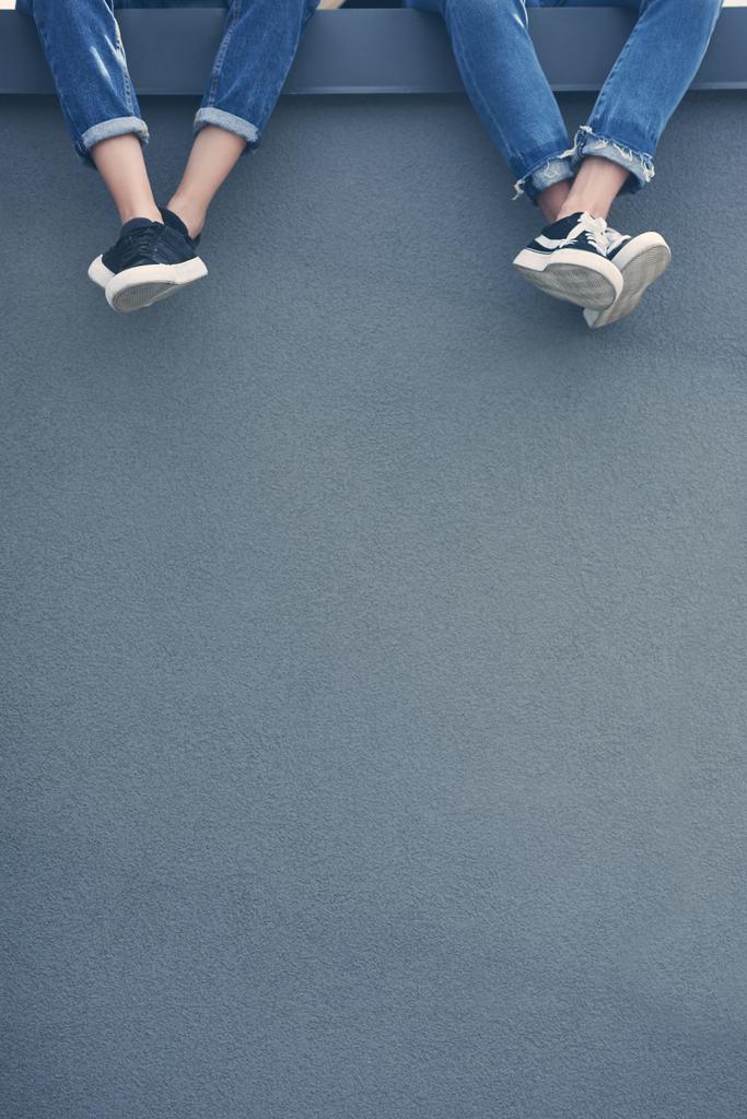 vista cortada de casal em jeans e tênis sentado na parede cinza
 - Foto, Imagem
