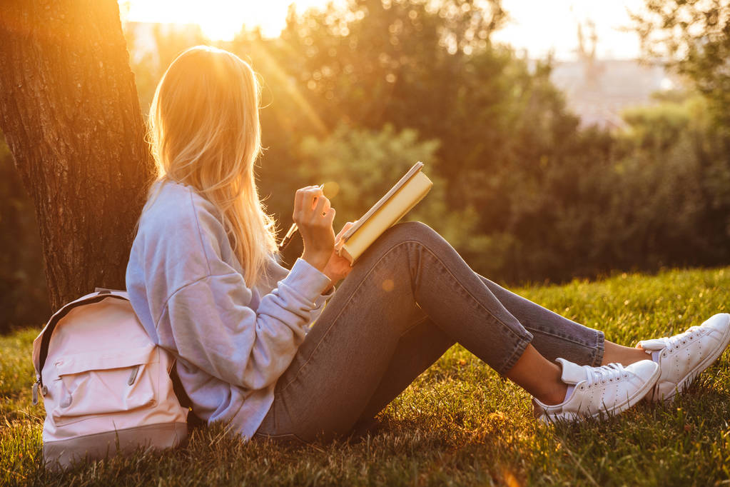 Portrait d'une jeune fille assise sur une herbe au parc, lisant un livre, prenant des notes
 - Photo, image