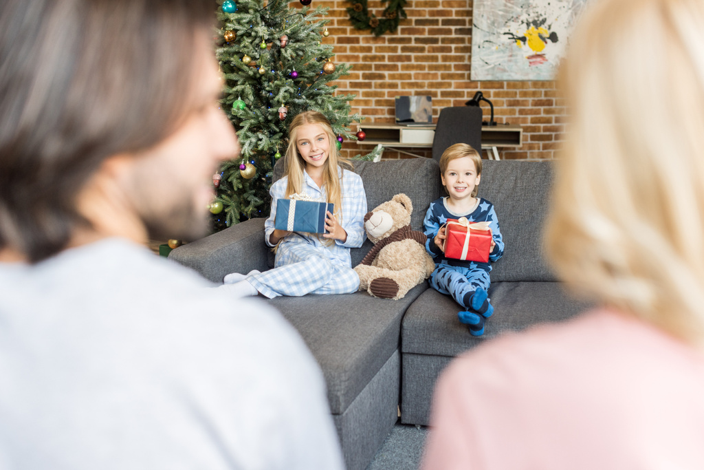 Selektywny fokus rodziców na pierwszym planie i szczęśliwe dzieci w piżamie gospodarstwa prezenty świąteczne   - Zdjęcie, obraz