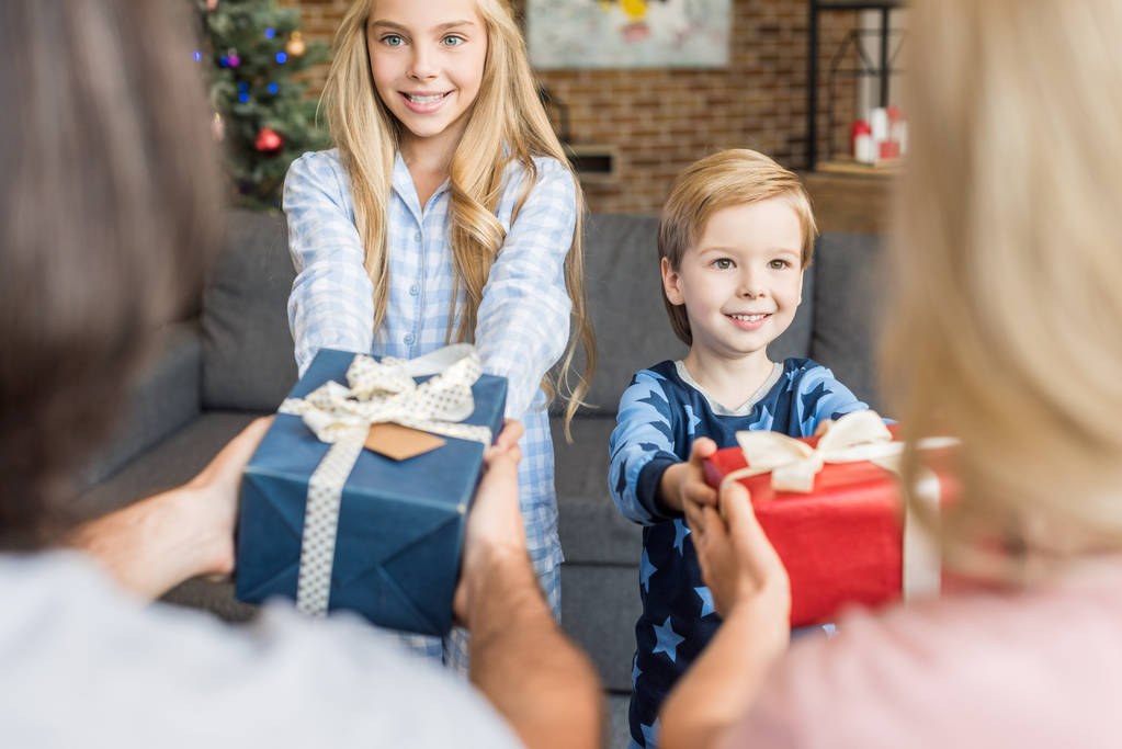 Schnappschuss von Eltern, die glücklichen Kindern Weihnachtsgeschenke im Pyjama präsentieren  - Foto, Bild