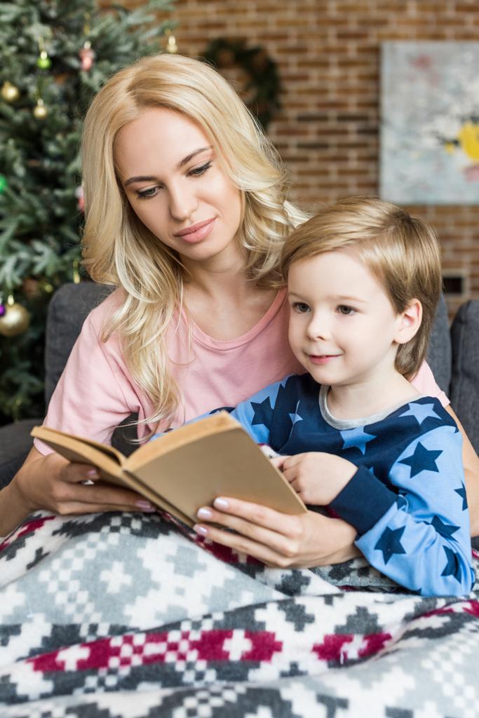 красивая молодая мать и восхитительный улыбающийся сын читают книгу вместе в разгар праздника
   - Фото, изображение