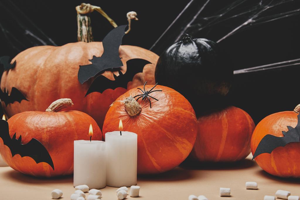 candles with flame, pumpkins, paper bats and scattered marshmallows on table, halloween concept - Photo, Image