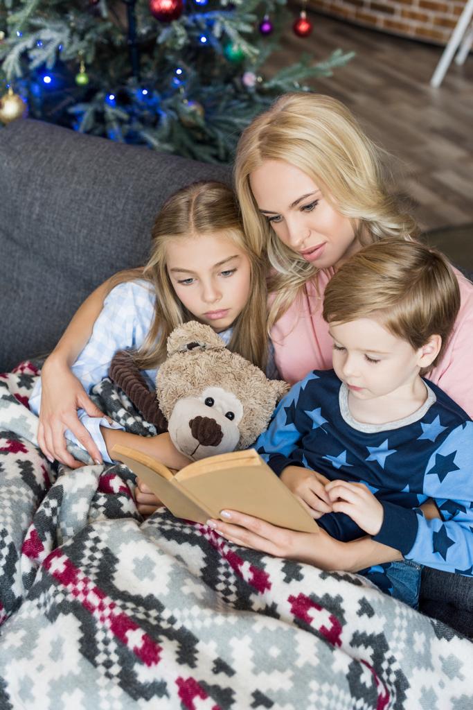 high angle view of young mother reading book with cute children in pajamas at christmas time  - Fotoğraf, Görsel
