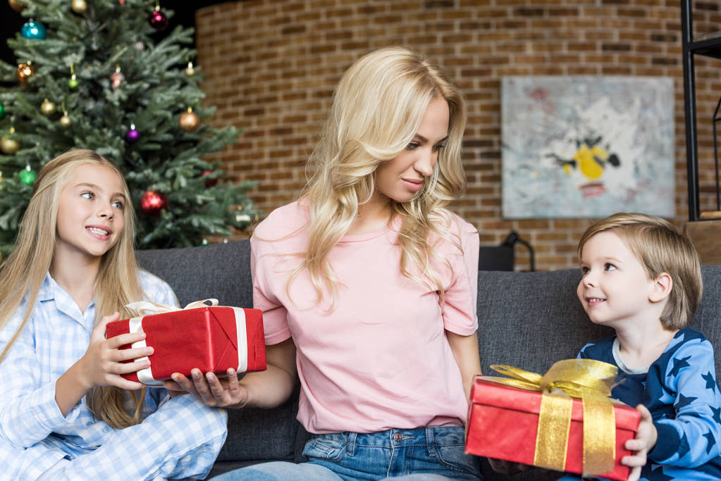 smiling young mother presenting christmas gifts to happy children in pajamas - Photo, Image