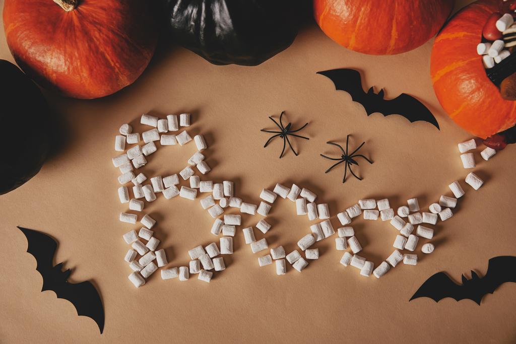 Hochwinkelaufnahme von Halloween-Kürbissen mit Papierfledermäusen und Wortbuh aus Marshmallows auf beigem Tisch - Foto, Bild