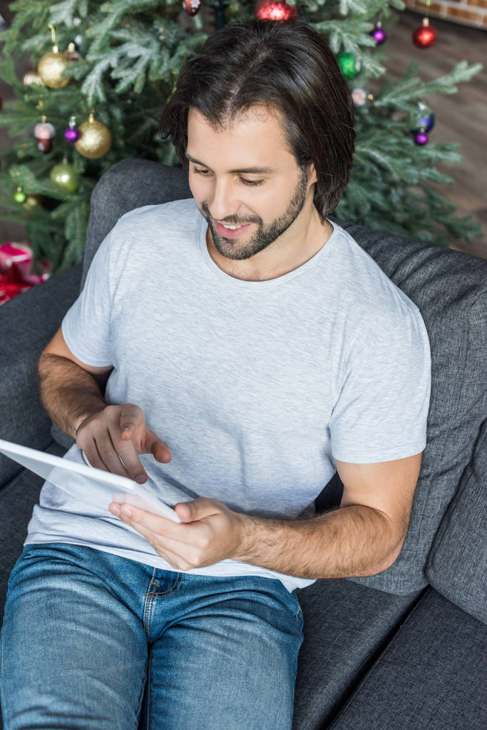 высокий угол обзора улыбающегося молодого человека с помощью цифрового планшета на Рождество
 - Фото, изображение