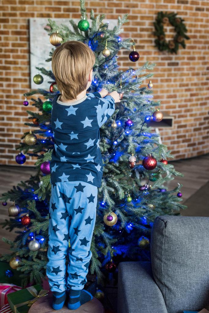назад вид милый маленький мальчик в пижаме украшая рождественскую елку
 - Фото, изображение