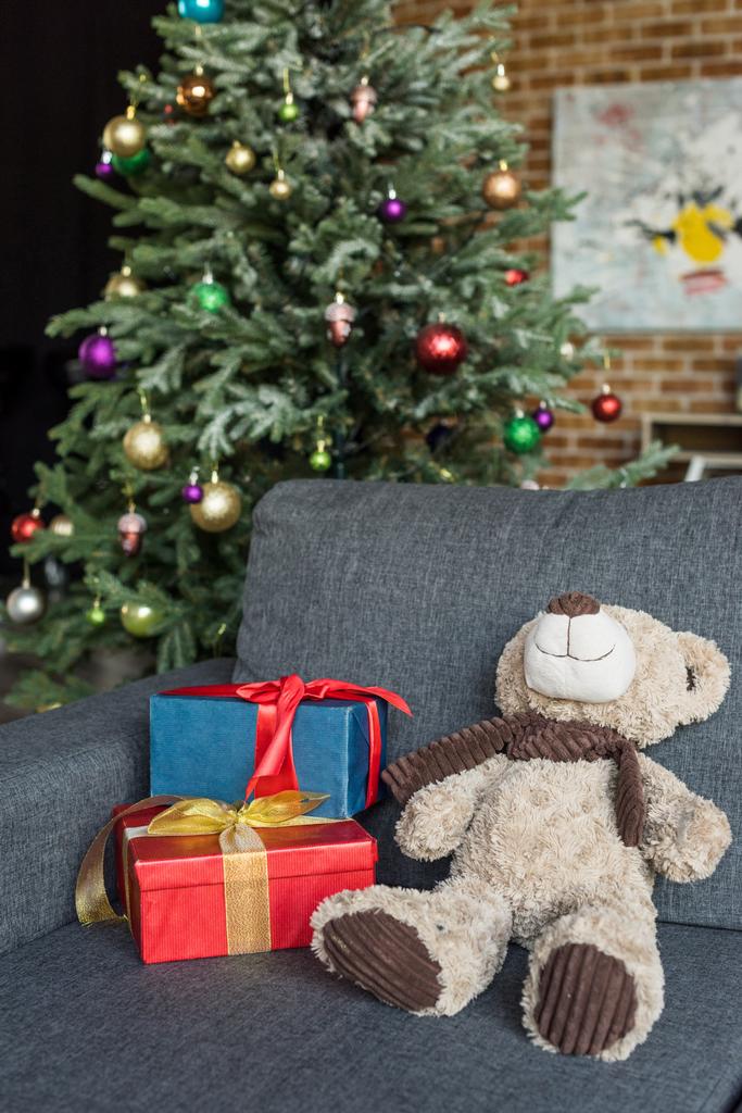 Medvídek s dárkové krabičky na gauč a zdobené vánoční strom za    - Fotografie, Obrázek