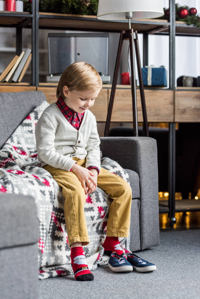 adorable niño feliz sentado en el sofá y mirando los zapatos
  - Foto, imagen