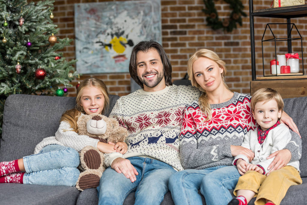 szczęśliwą rodziną, dwie urocze dzieci siedzi na kanapie i uśmiechając się aparatu w czasie świąt Bożego Narodzenia  - Zdjęcie, obraz