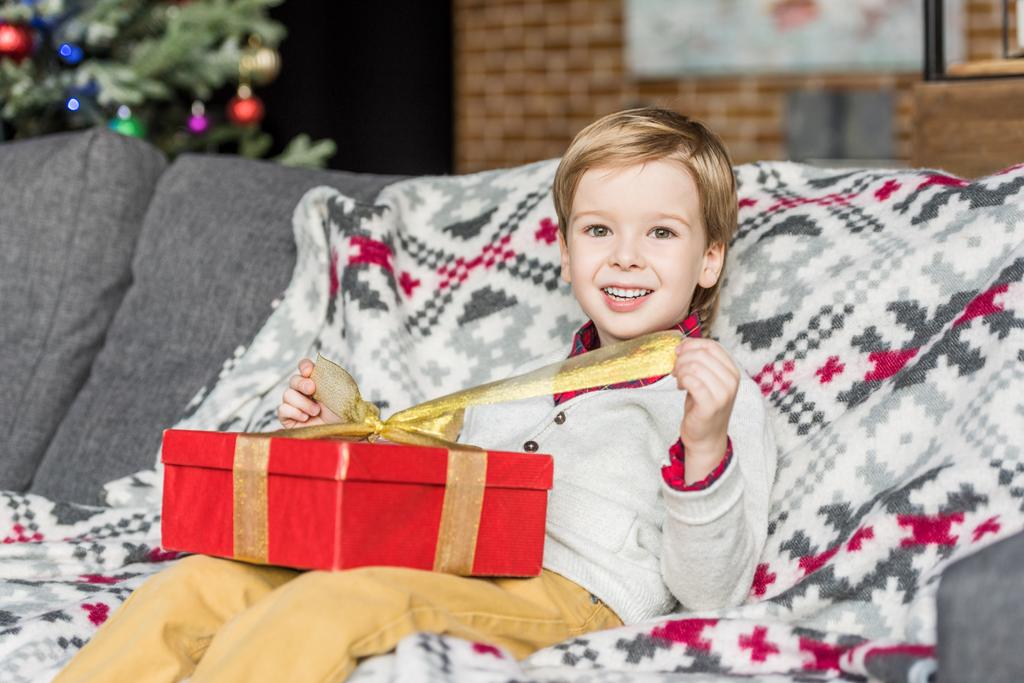 cute happy little boy opening christmas gift and smiling at camera - Photo, Image