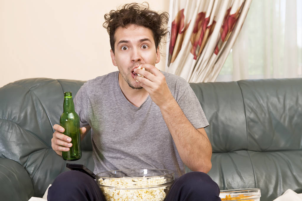 Uomo con birra e patatine guardando la TV a casa
 - Foto, immagini