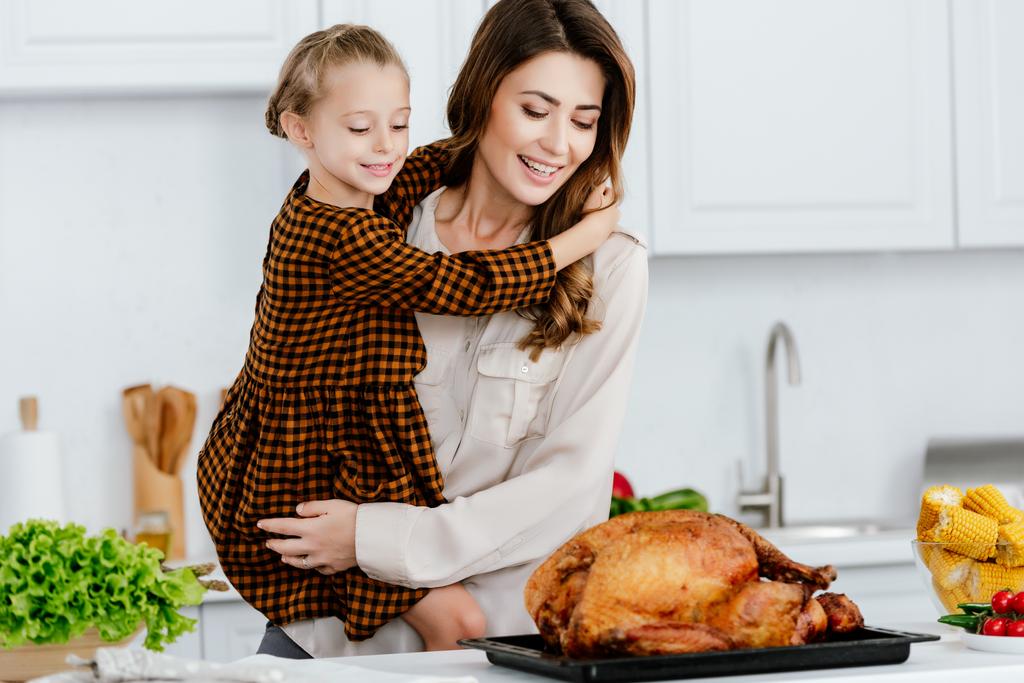 beautiful young mother and daughter embracing and looking at thanksgiving turkey - Photo, Image