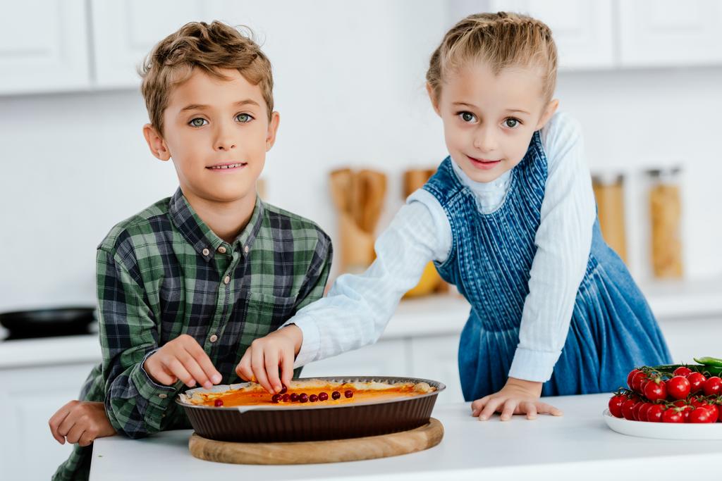 братья и сестры украшают тыквенный пирог ягодами вместе на кухне
 - Фото, изображение