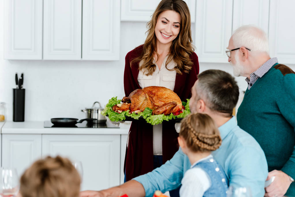  donna sorridente che porta tacchino al forno per la cena del Ringraziamento con la famiglia
  - Foto, immagini