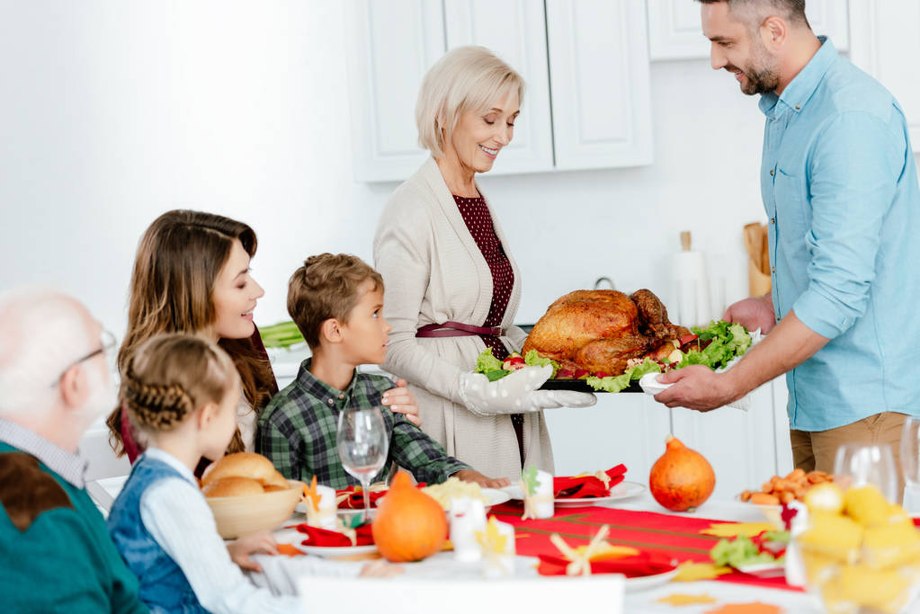 femme âgée et homme adulte portant la dinde cuite au four pour le dîner de Thanksgiving avec la famille à la maison
 - Photo, image