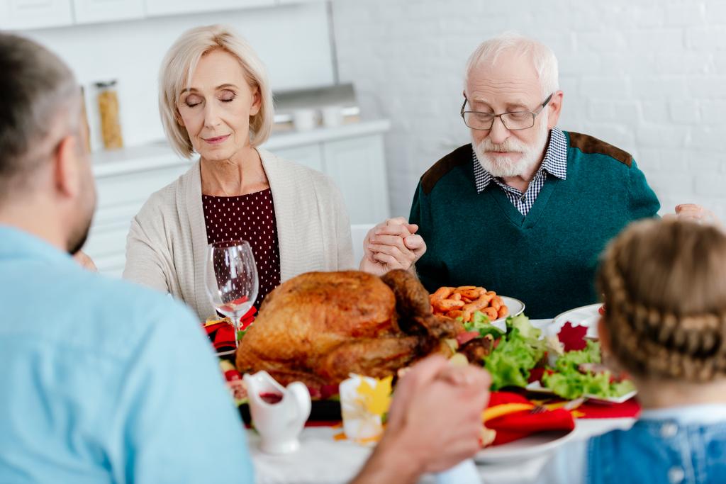 Senior para z rodziny modląc się przy stole serwowane z Turcją przed kolacja wakacje na Święto Dziękczynienia  - Zdjęcie, obraz