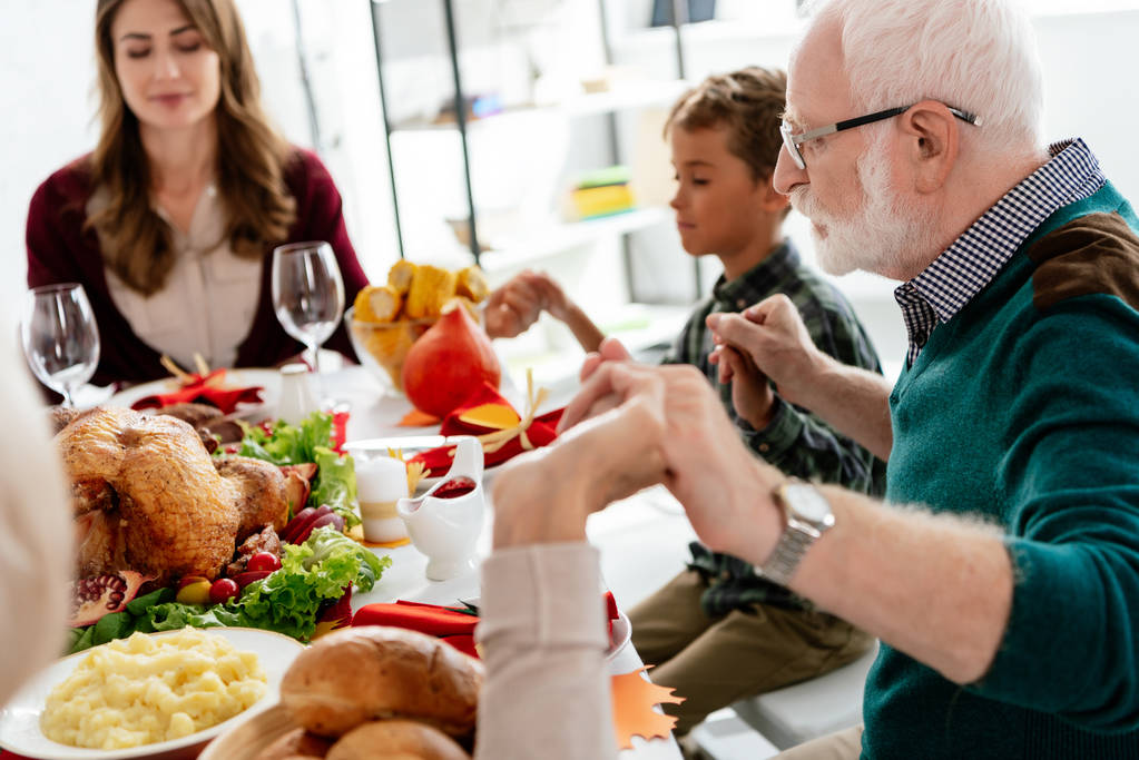 感謝祭の休日の夕食の前にトルコと役立ったテーブルで祈っている幸せな家族  - 写真・画像