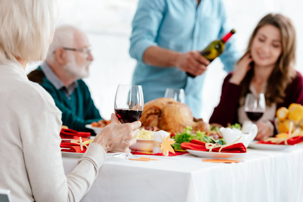 vista parcial de la mujer mayor con copa de vino celebrando acción de gracias con la familia en la mesa servida con pavo
  - Foto, imagen