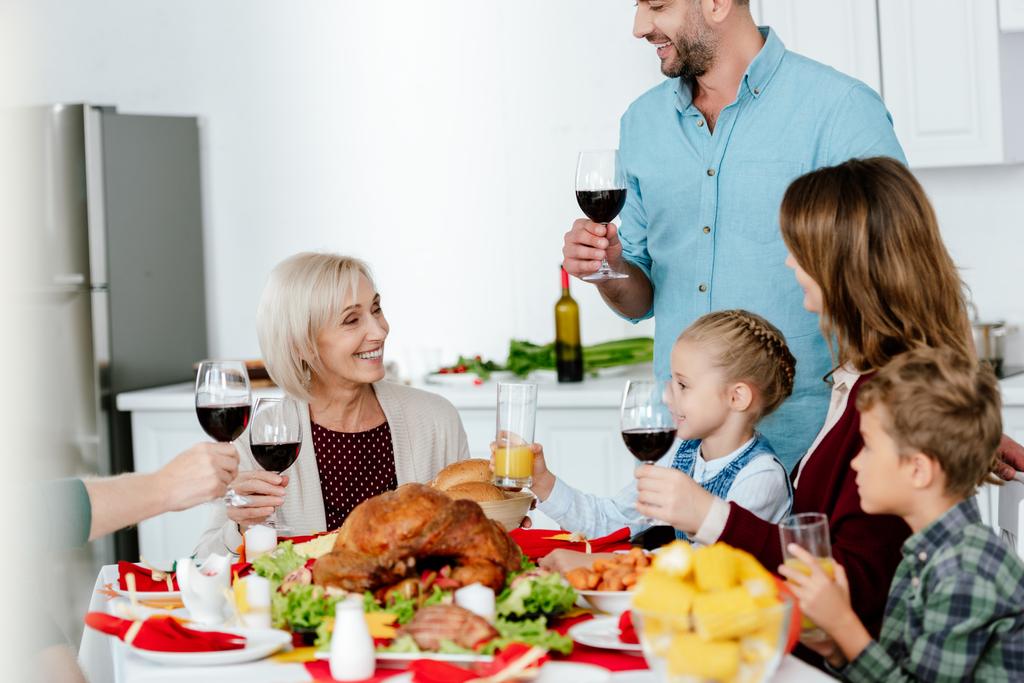 partial view of adult man with wine glass making toast at served table with turkey while his family celebrating thanksgiving  - Photo, Image