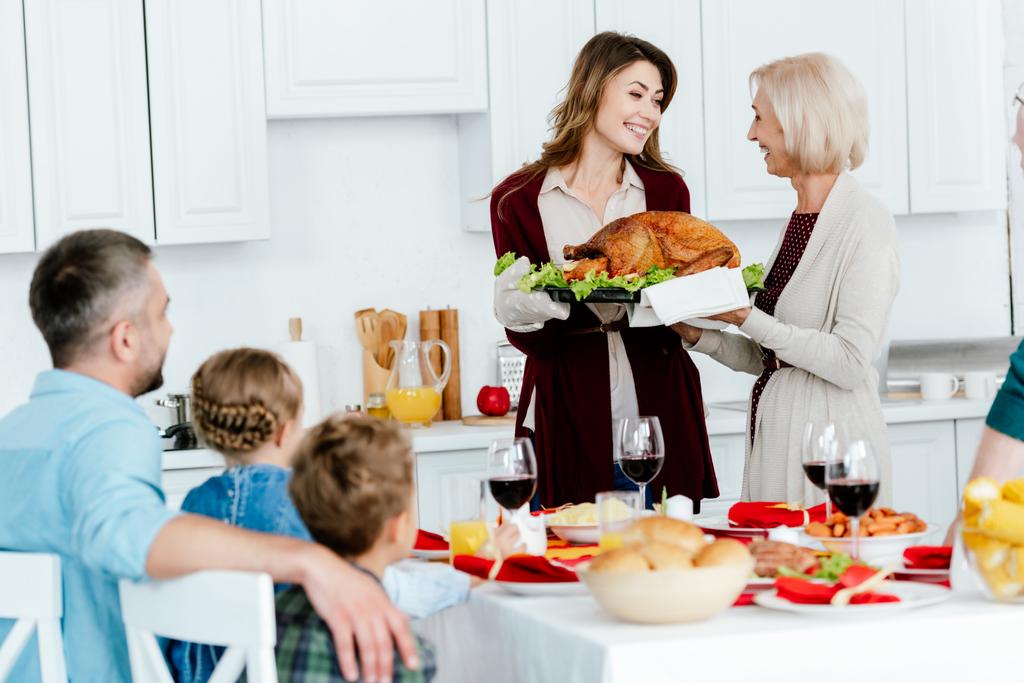 vanhempi nainen kuljettaa kalkkunaa aikuisen tyttären kanssa kiitospäivän illalliselle perheen kanssa kotona
  - Valokuva, kuva