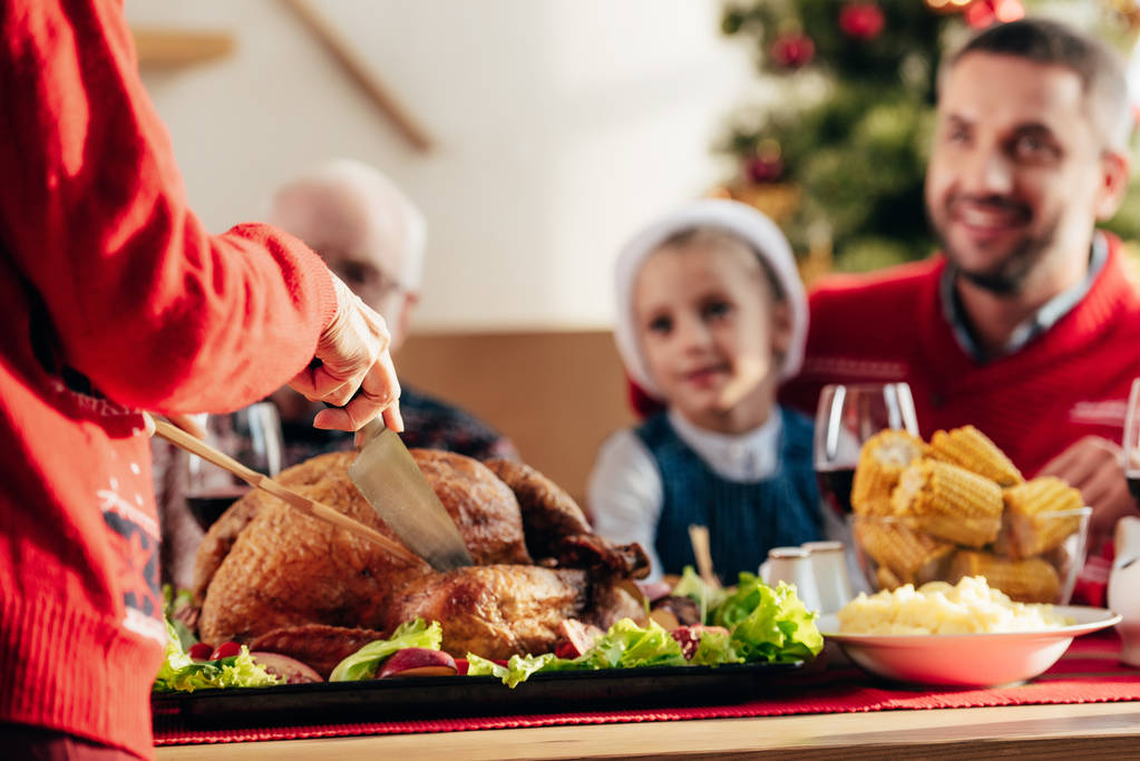 przycięty obraz kobiety krojenie pysznych Tukeya świąteczną kolację wigilijną i szczęśliwa Rodzina w domu - Zdjęcie, obraz