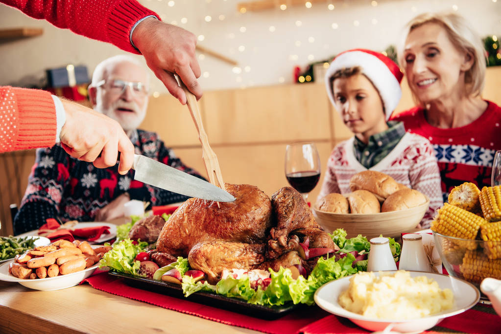 partial view of man slicing holiday turkey for christmas celebration with happy family at home  - Photo, Image