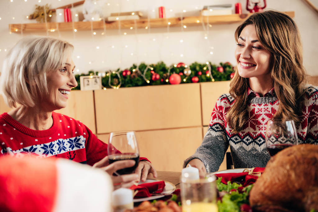 Senior lächelnde Frau mit Weinglas feiert Weihnachten mit erwachsener Tochter zu Hause  - Foto, Bild