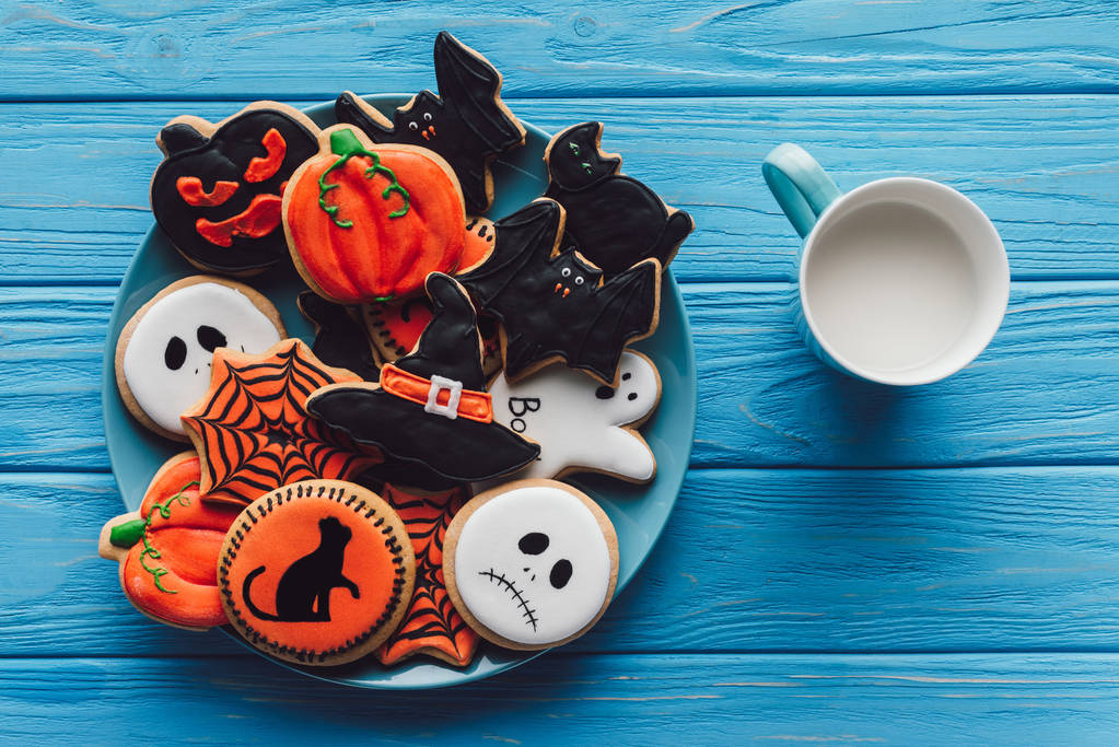 Blick von oben auf Tasse mit Milch und Teller mit hausgemachten Halloween-Plätzchen auf Holztisch  - Foto, Bild
