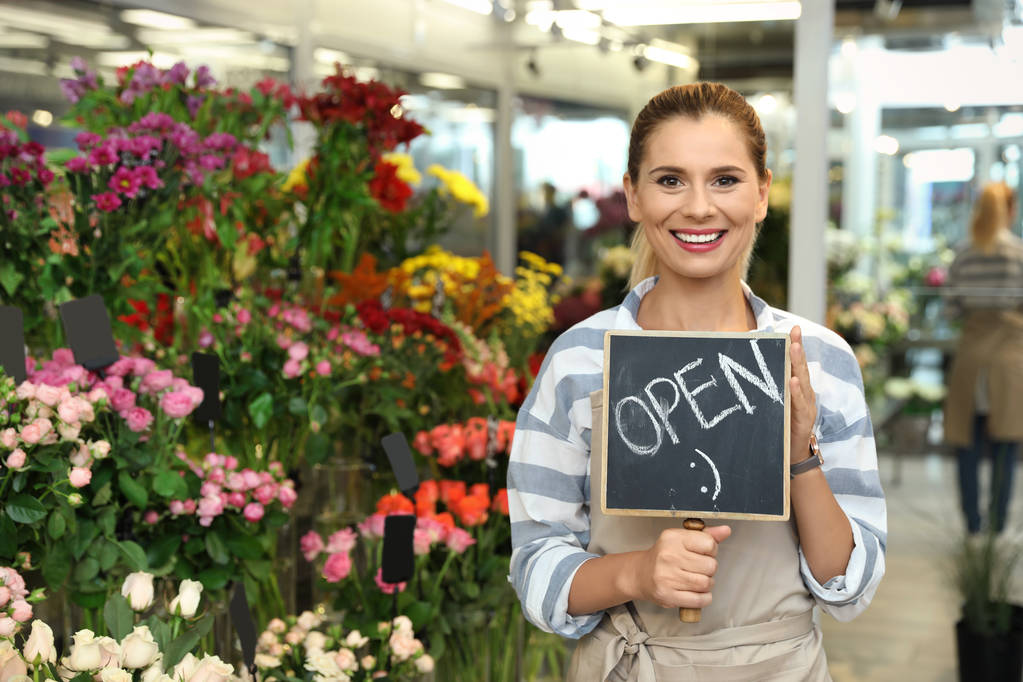 Floristería femenina sosteniendo el cartel "OPEN" en la tienda de flores
 - Foto, Imagen
