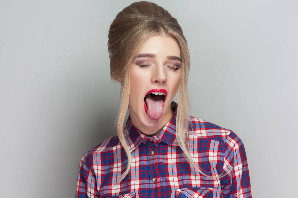 divertida mujer rubia con la boca abierta y la lengua sobre fondo gris
 - Foto, Imagen
