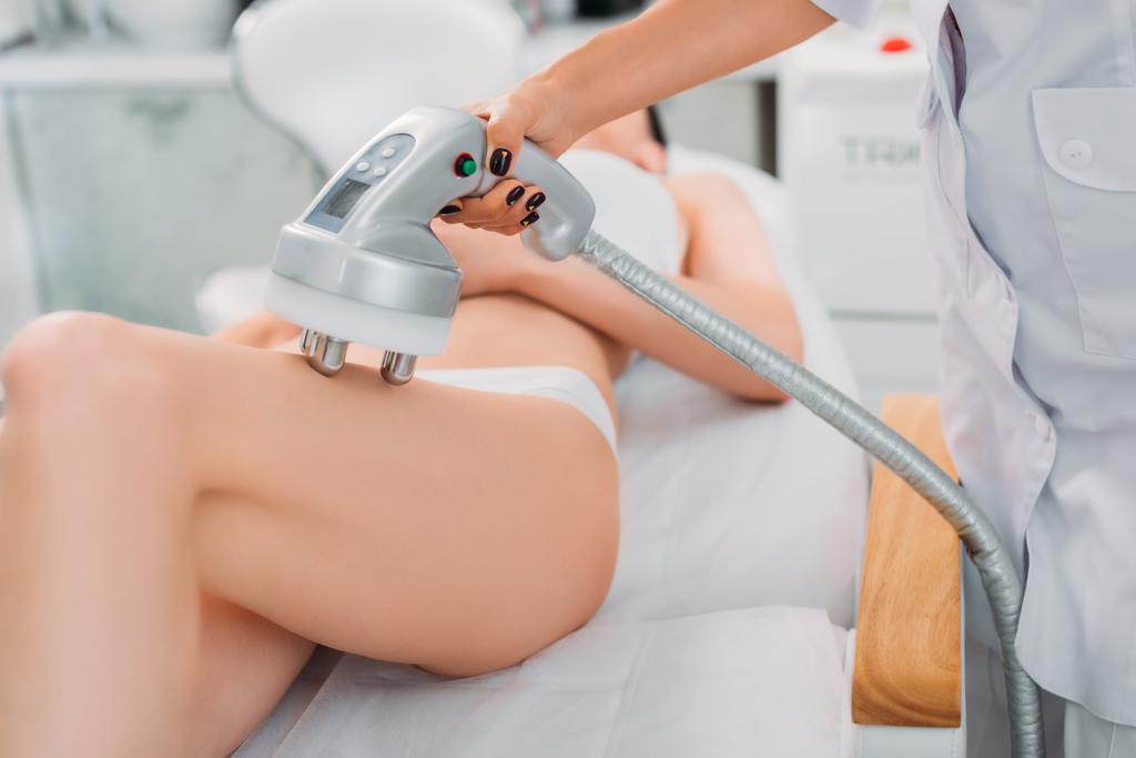 gedeeltelijke weergave van schoonheidsspecialist maken elektrische massage aan vrouwelijke client in wit ondergoed in spa salon - Foto, afbeelding