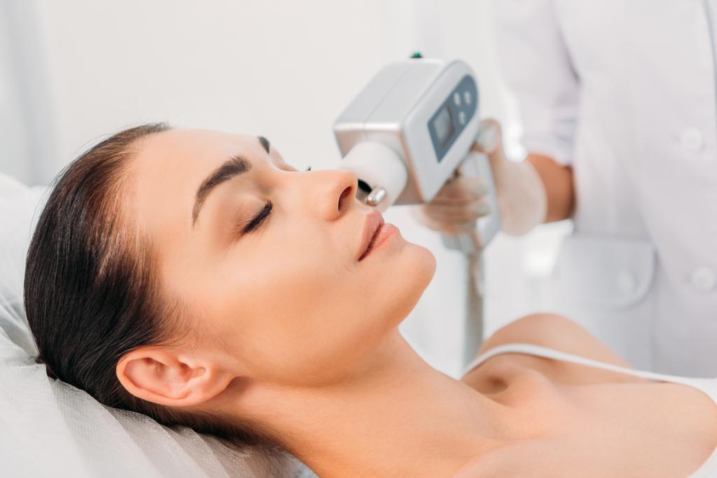 gedeeltelijke weergave van mooie vrouw krijgen gezicht stimuleren elektrische massage van de schoonheidsspecialist in de Wellness salon - Foto, afbeelding