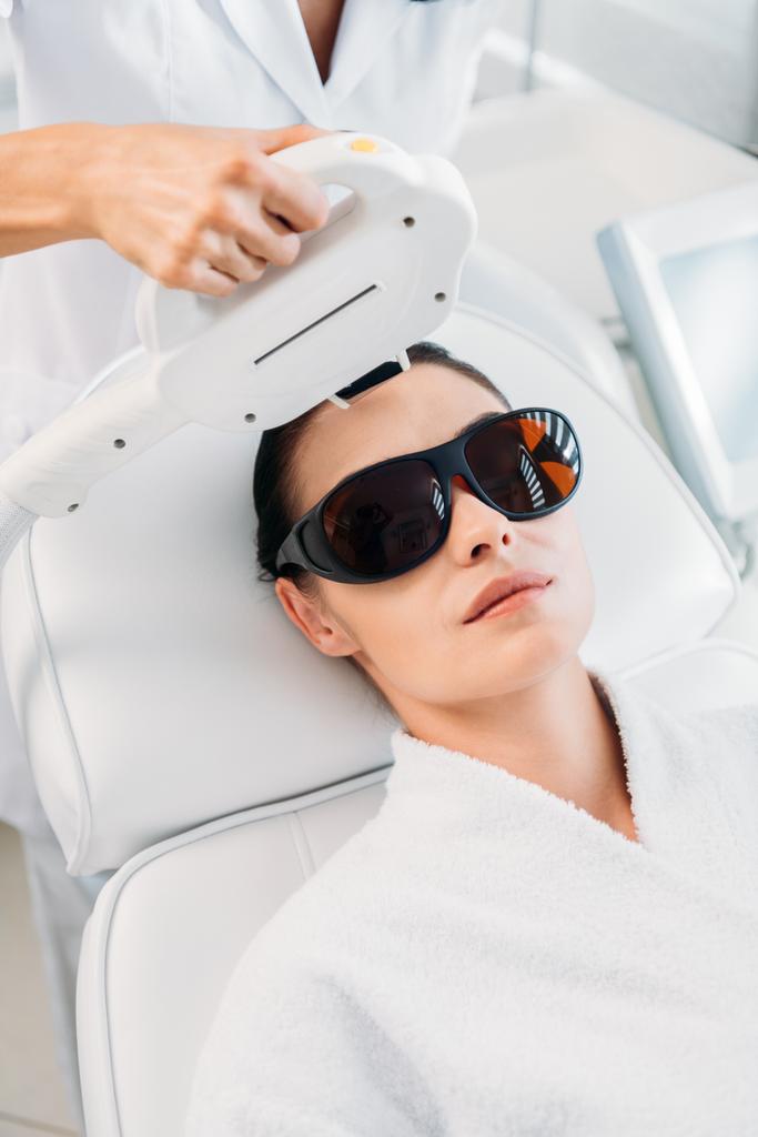 женщина в защитных очках, получающая лазерную эпиляцию, сделанную косметологом в спа-салоне
 - Фото, изображение
