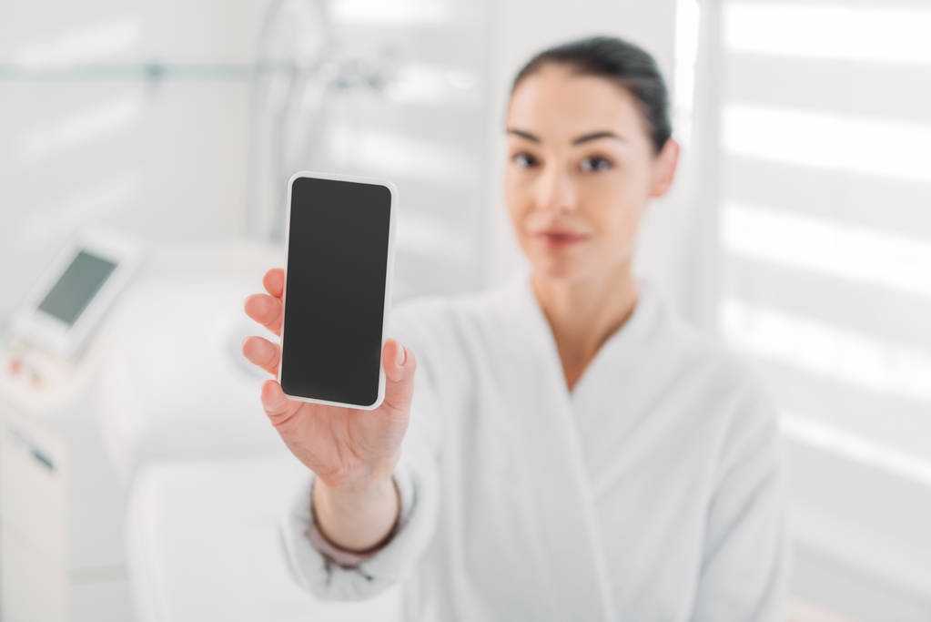 Žena v bílém županu ukazující smartphone s prázdnou obrazovkou ve spa salonu  - Fotografie, Obrázek