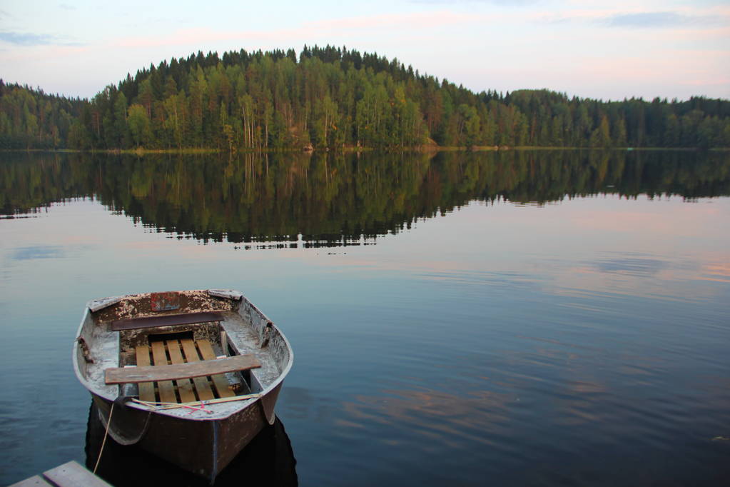 hermosa foto con vista al lago con agua casi suave, barco atado, bosque en el otro lado, reflejo del cielo en el agua, tonos azules rosados, noche
 - Foto, imagen