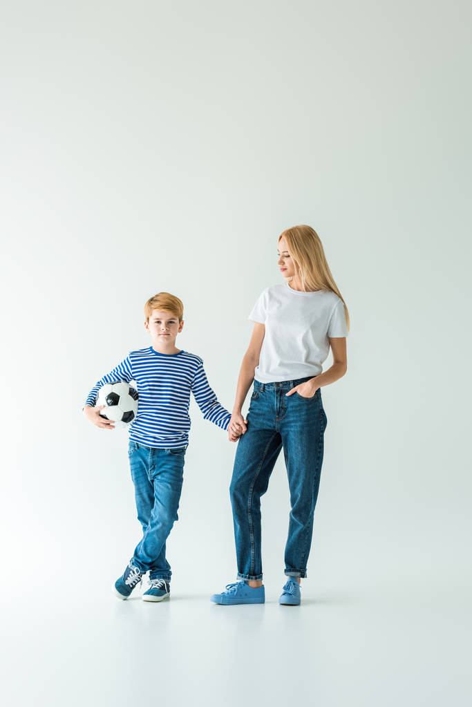 madre e figlio in piedi con pallone da calcio e tenendosi per mano sul bianco
 - Foto, immagini