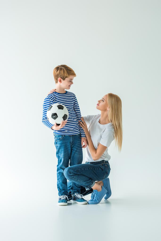 μητέρα οκλαδόν κοντά γιος με μπάλα ποδοσφαίρου σε λευκό - Φωτογραφία, εικόνα