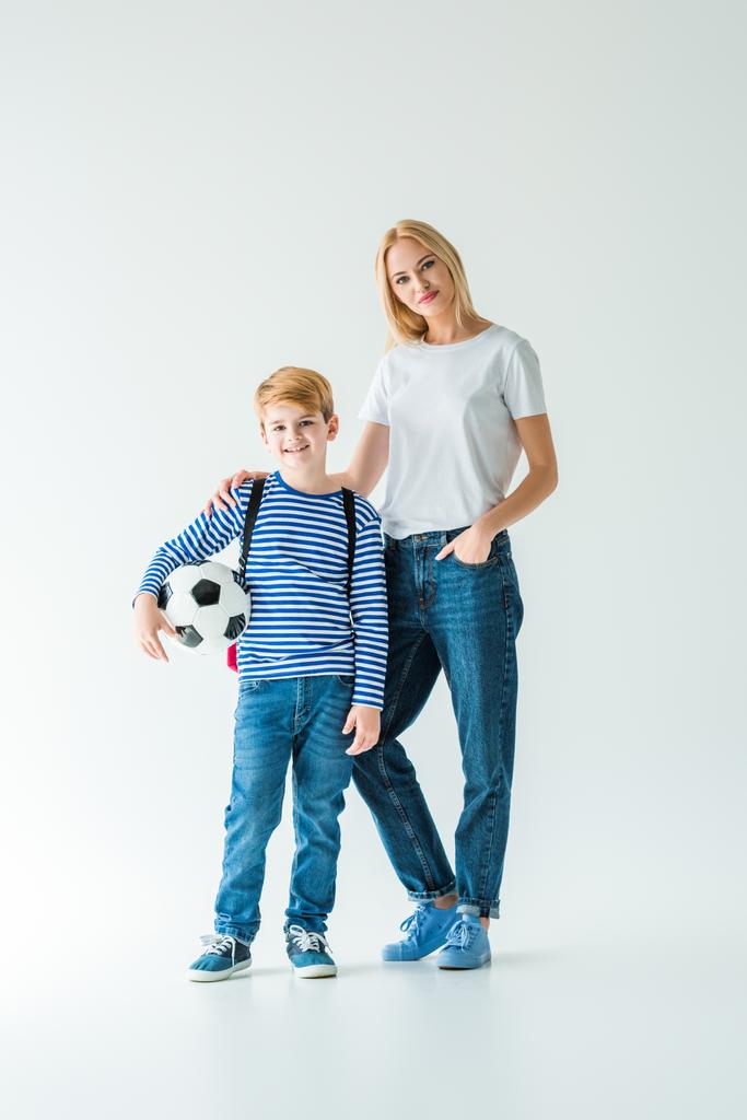 vrolijke moeder en zoon permanent met voetbal bal op wit en camera te kijken - Foto, afbeelding