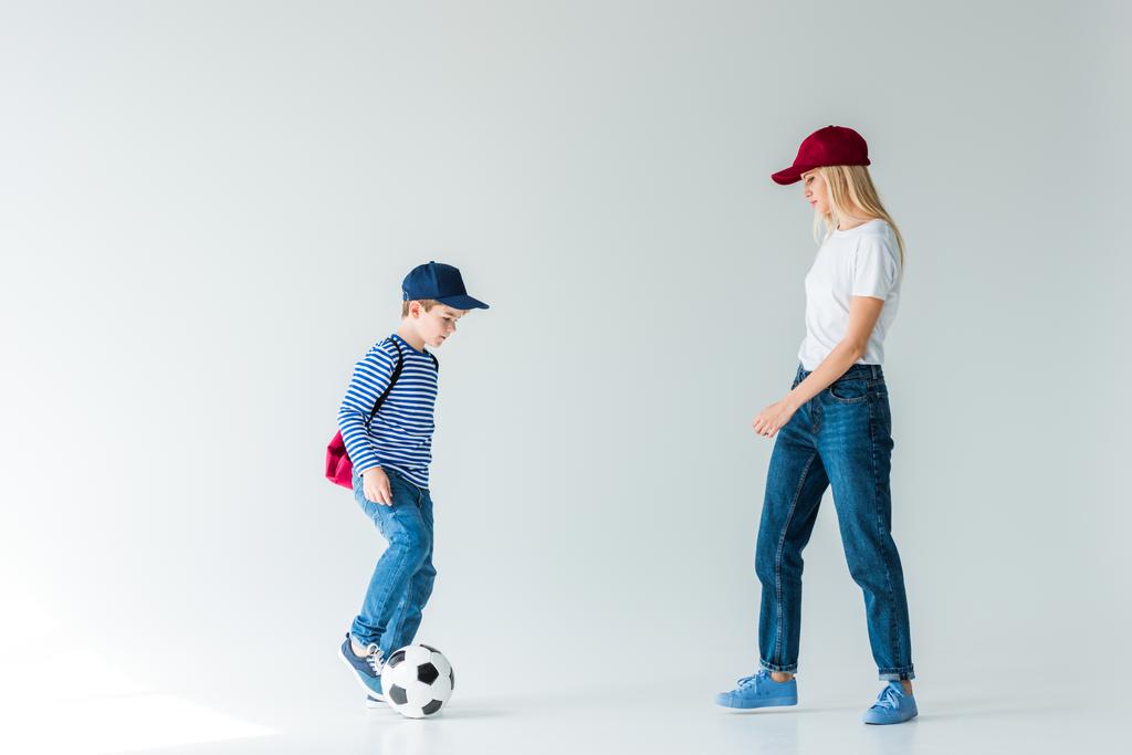 visão lateral de mãe e filho com mochila brincando com bola de futebol no branco
 - Foto, Imagem