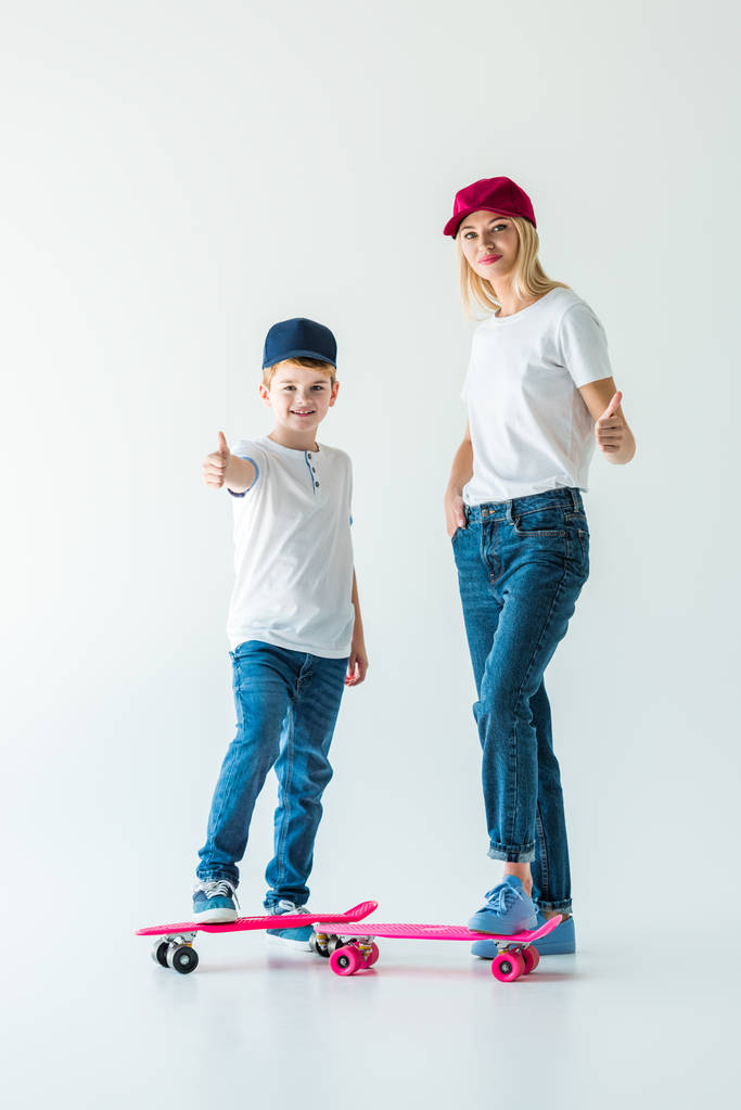 улыбающиеся мать и сын в шапках, стоящие рядом с коньками и показывающие большие пальцы на белом
 - Фото, изображение